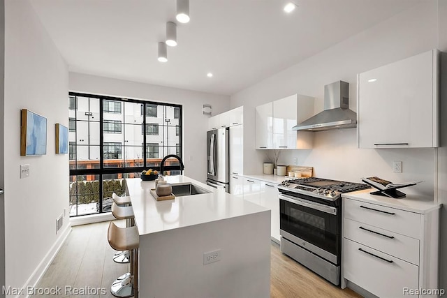 kitchen featuring a sink, modern cabinets, appliances with stainless steel finishes, and wall chimney range hood