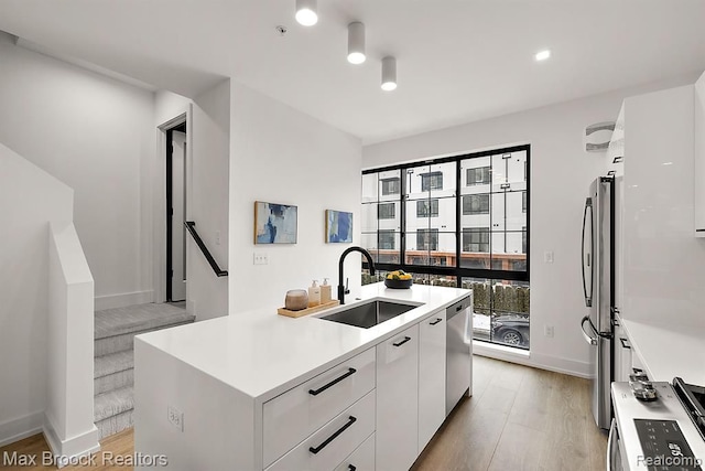 kitchen with a sink, white cabinets, light wood-style floors, appliances with stainless steel finishes, and modern cabinets