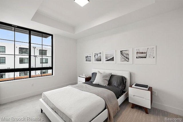 bedroom featuring baseboards, a raised ceiling, and multiple windows