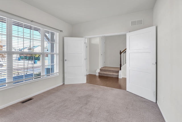 unfurnished room featuring carpet floors, visible vents, stairway, and baseboards