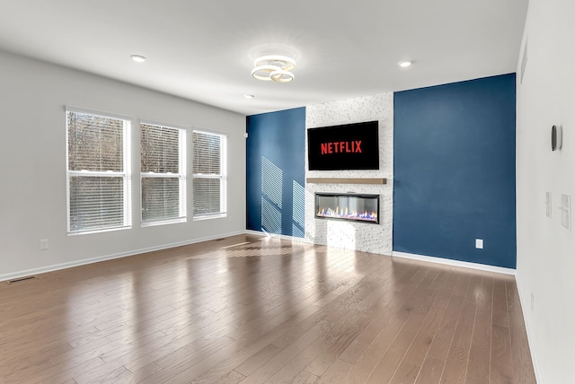 unfurnished living room featuring a fireplace, wood finished floors, visible vents, and baseboards