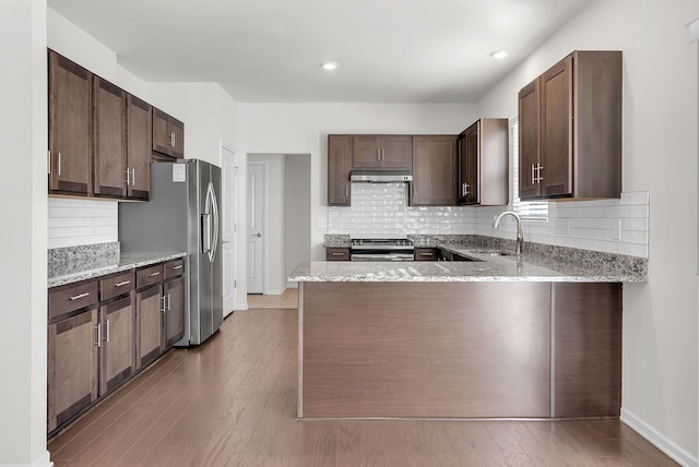 kitchen with appliances with stainless steel finishes, a sink, dark brown cabinetry, light stone countertops, and under cabinet range hood