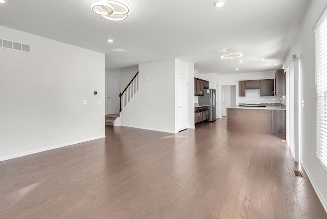 unfurnished living room with baseboards, visible vents, stairway, dark wood-style flooring, and a sink