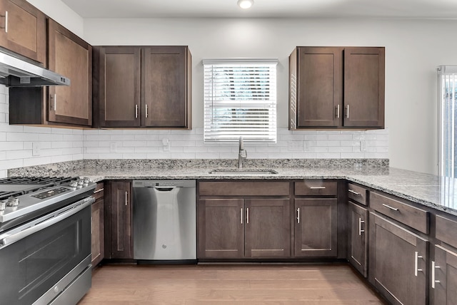 kitchen with stainless steel appliances, range hood, a sink, and light wood finished floors