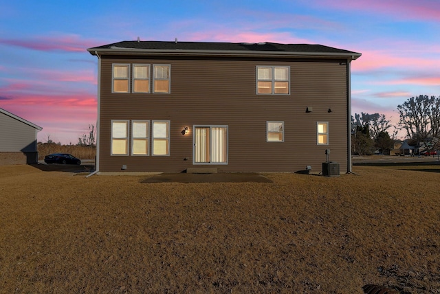 rear view of house with central AC and a lawn