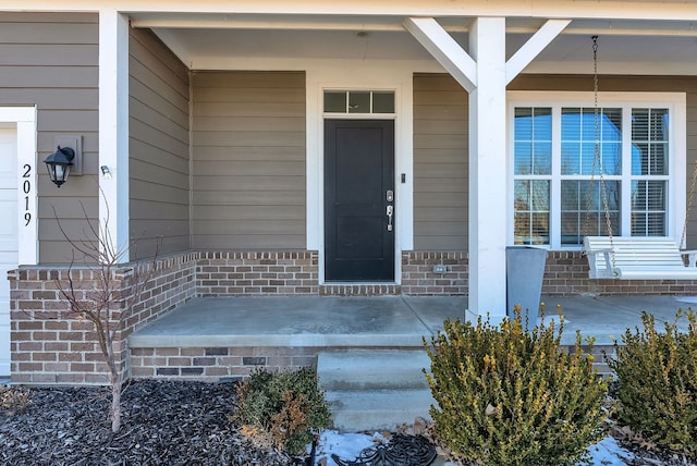 doorway to property with a porch and brick siding