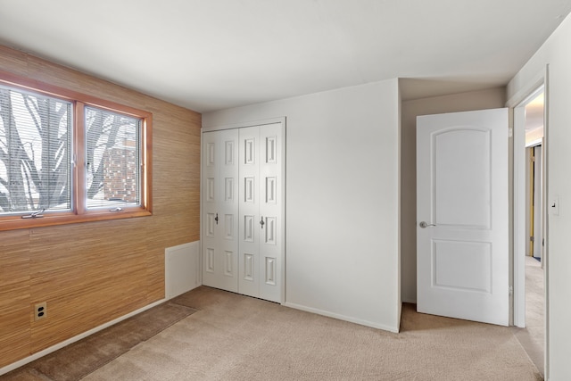 unfurnished bedroom featuring a closet, wood walls, and light colored carpet