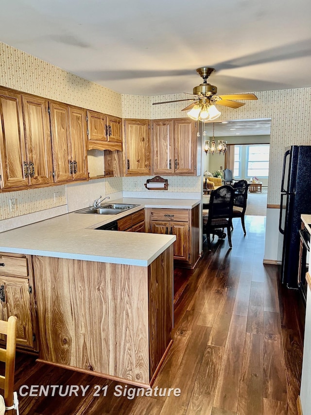 kitchen with sink, black fridge, dark hardwood / wood-style floors, kitchen peninsula, and ceiling fan with notable chandelier