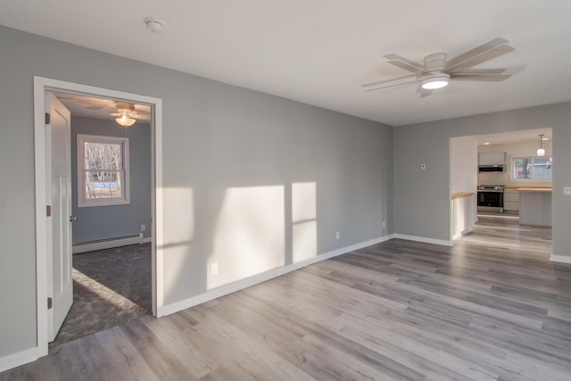 unfurnished living room with a baseboard heating unit, ceiling fan, and light wood-type flooring