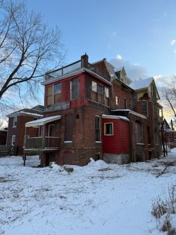 snow covered rear of property featuring a chimney