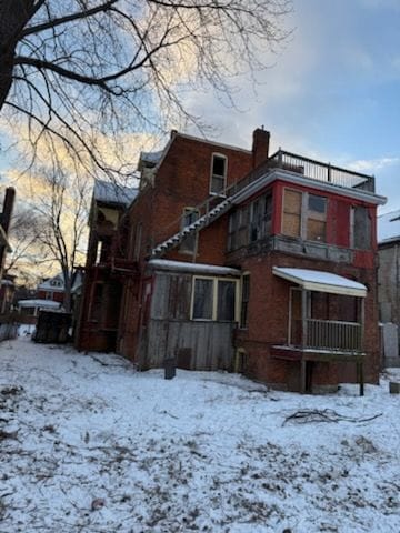 snow covered back of property featuring a chimney