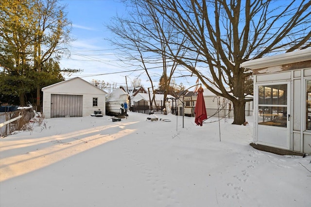 snowy yard with a detached garage, fence, and an outdoor structure