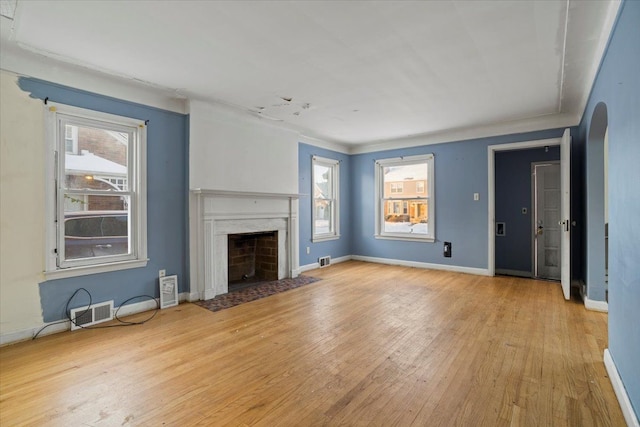 unfurnished living room with light wood-style floors, arched walkways, plenty of natural light, and a premium fireplace