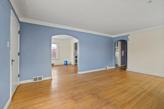 empty room featuring baseboards, visible vents, arched walkways, ornamental molding, and wood finished floors