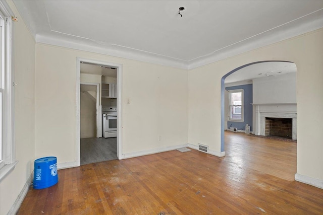 unfurnished room featuring baseboards, visible vents, arched walkways, wood finished floors, and a fireplace