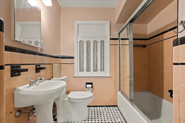 bathroom featuring a wainscoted wall, tile walls, toilet, enclosed tub / shower combo, and tile patterned floors