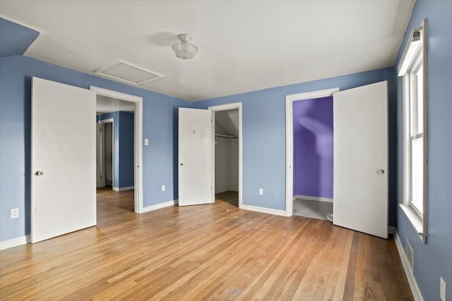 unfurnished bedroom with baseboards, two closets, attic access, and light wood-style floors