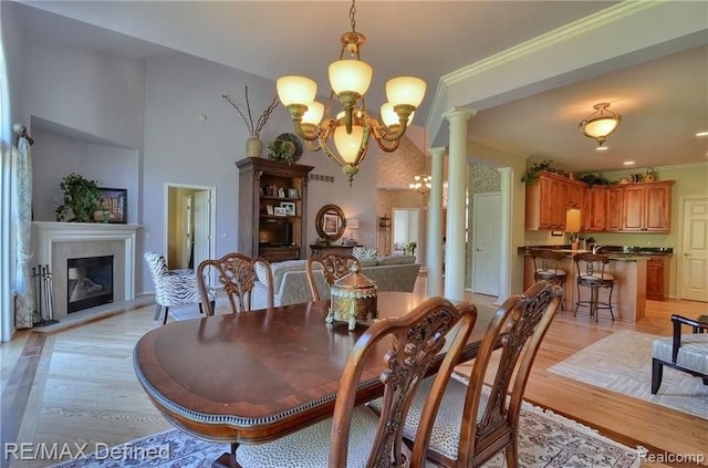 dining space with ornate columns, crown molding, a fireplace, and light hardwood / wood-style floors