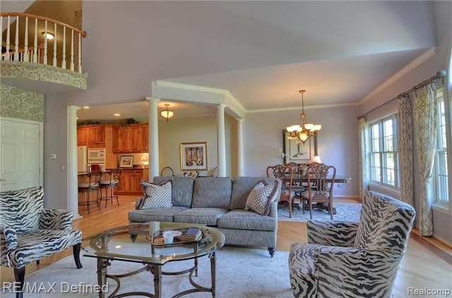 living room with decorative columns, crown molding, a chandelier, and light hardwood / wood-style flooring