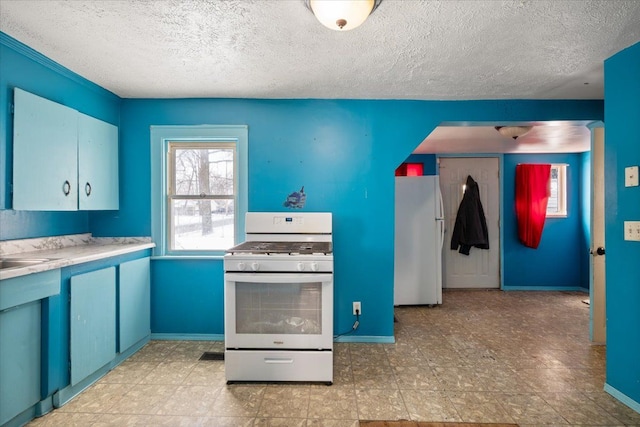 kitchen with light countertops, a textured ceiling, blue cabinets, white appliances, and baseboards