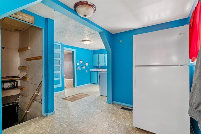 kitchen featuring visible vents, baseboards, a textured ceiling, and freestanding refrigerator