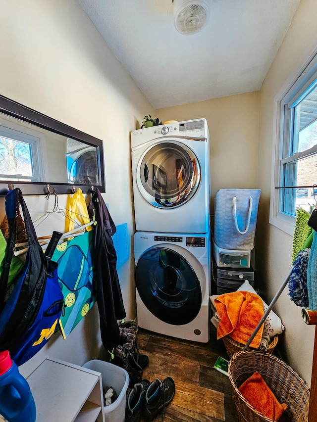 clothes washing area featuring stacked washer and dryer, a healthy amount of sunlight, and dark hardwood / wood-style floors