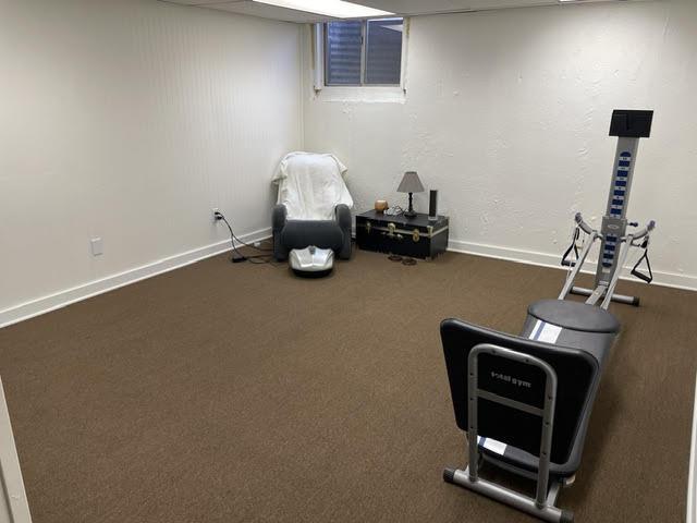 workout room featuring dark carpet and baseboards