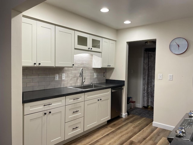 kitchen with glass insert cabinets, dark countertops, a sink, and dishwasher