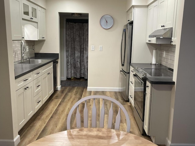 kitchen featuring stainless steel appliances, dark countertops, glass insert cabinets, white cabinetry, and under cabinet range hood