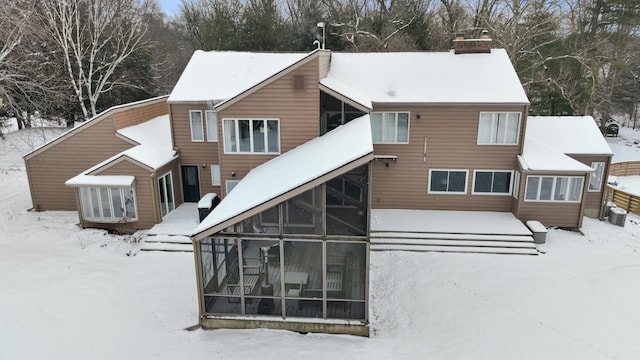 snow covered rear of property with a sunroom and a chimney