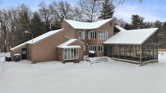 snow covered rear of property featuring a sunroom