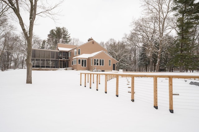 snow covered back of property featuring a sunroom and a chimney