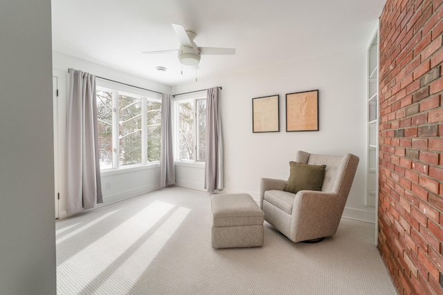 living area with carpet, ceiling fan, and brick wall