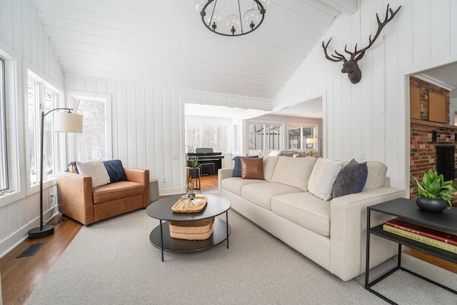 living area featuring a chandelier, visible vents, vaulted ceiling, and wood finished floors