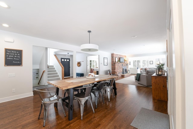 dining space with dark wood-type flooring, a fireplace, baseboards, and stairs