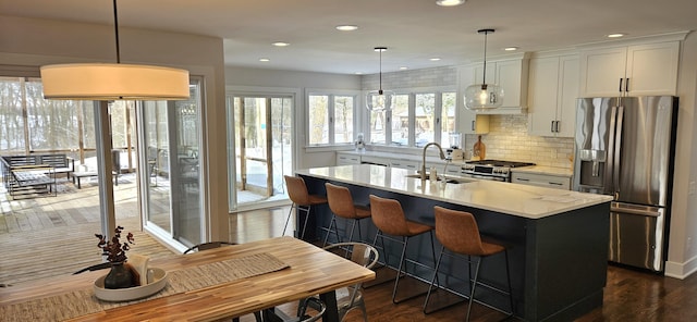 kitchen featuring a kitchen island with sink, white cabinets, light countertops, appliances with stainless steel finishes, and decorative light fixtures