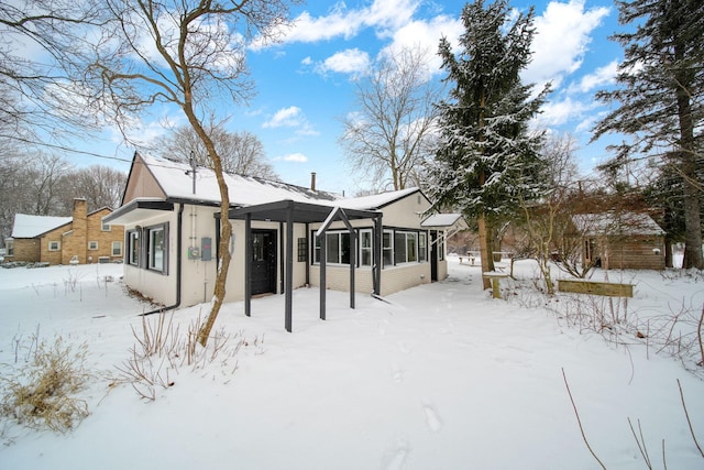 snow covered rear of property featuring a sunroom