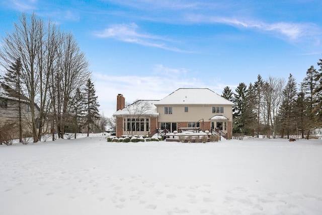 snow covered rear of property with a chimney and brick siding