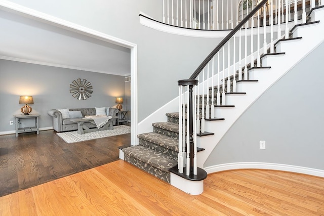 stairs with crown molding, a high ceiling, baseboards, and wood finished floors