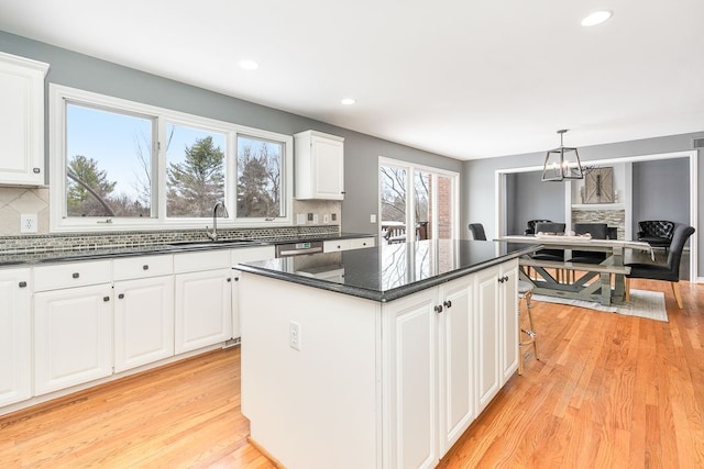 kitchen featuring white cabinets, decorative light fixtures, a kitchen island, and a sink