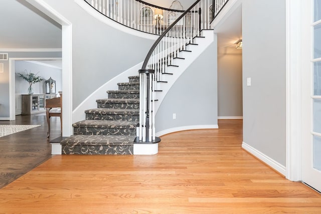 stairway featuring baseboards, visible vents, a towering ceiling, ornamental molding, and wood finished floors