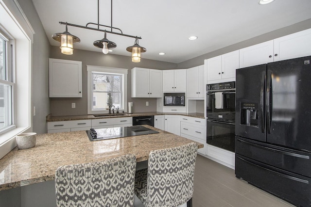 kitchen featuring sink, white cabinetry, light stone counters, hanging light fixtures, and black appliances