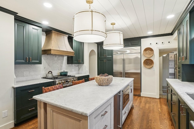 kitchen featuring premium range hood, a kitchen island, pendant lighting, tasteful backsplash, and built in appliances