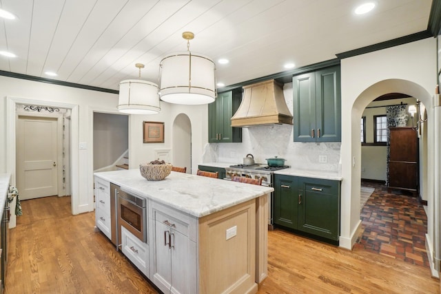 kitchen featuring custom exhaust hood, light stone counters, hanging light fixtures, stainless steel microwave, and a kitchen island