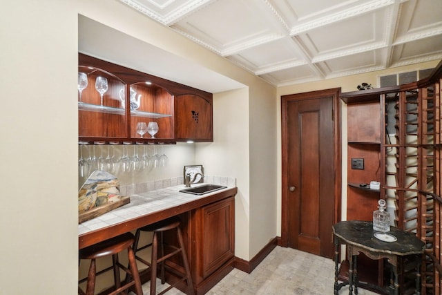 bar featuring coffered ceiling, sink, and tile counters