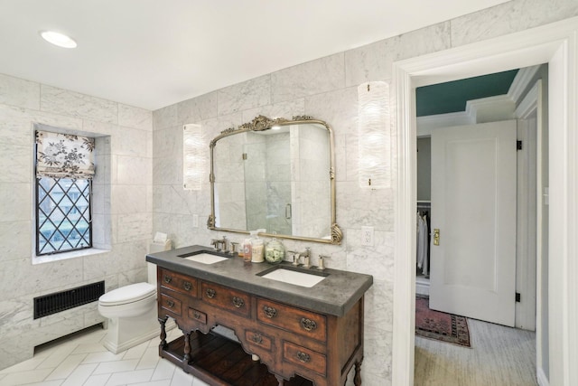 bathroom with a shower with door, vanity, tile walls, and toilet