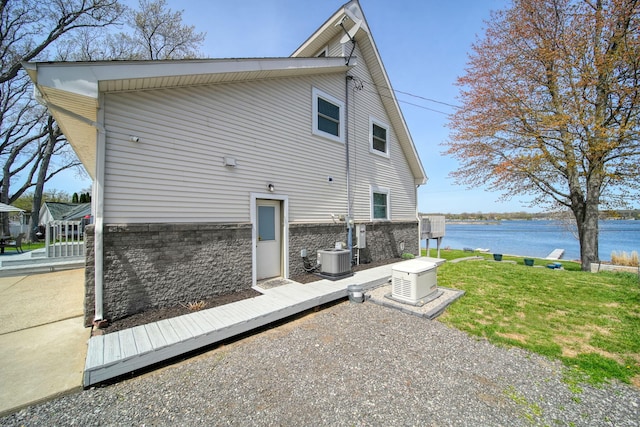 exterior space featuring brick siding, a water view, central AC unit, and a lawn