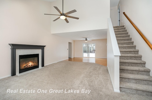 unfurnished living room featuring ceiling fan, a towering ceiling, and carpet flooring