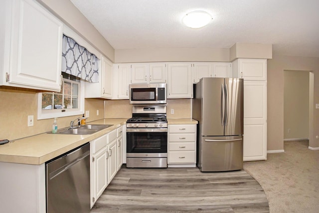 kitchen with stainless steel appliances, white cabinetry, sink, and light wood-type flooring