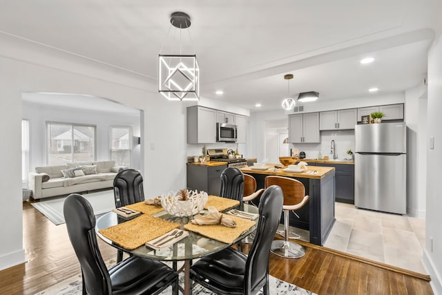 dining space featuring light wood finished floors, baseboards, arched walkways, and recessed lighting